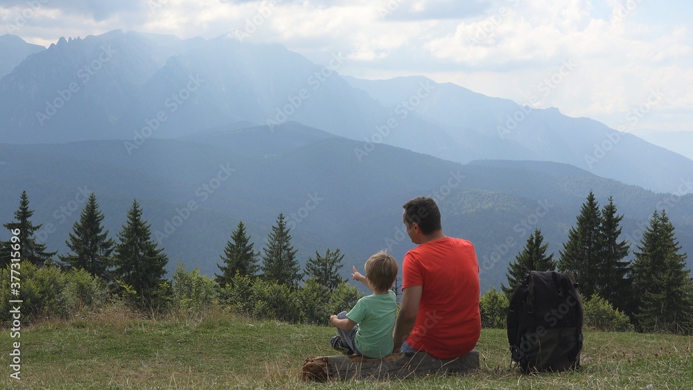 Father and son sit and look at mountains top, holiday in nature, sun rays shine