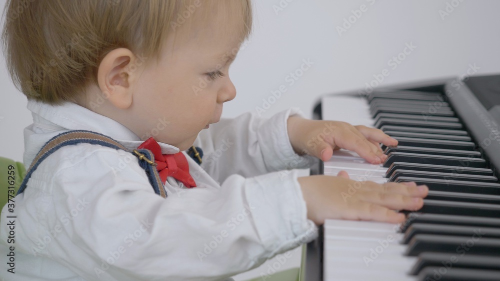 Funny little baby child play passionate at piano, elegant boy with blue eyes and blond hair, elegant boy with red bow Funny little baby child play passionate at piano, elegant boy with blue eyes and blond hair, elegant boy with red bow