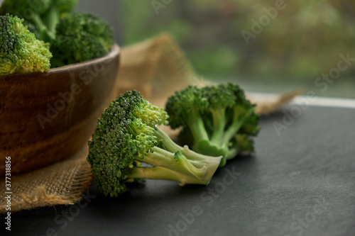 Fresh Broccoli in wooden bowl and seed oil in rustic style. Close up on a black background. side view, harvest cruciferous copy space for text.