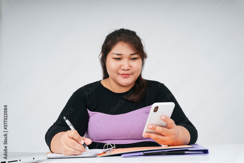 Asian chubby business woman working at desk holding smartphone. Asian chubby business woman working at desk holding smartphone.