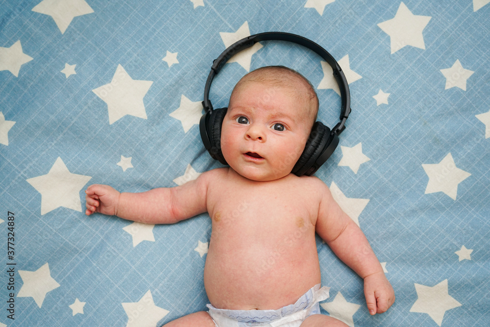Bebé con auriculares escuchando música en una cama blanca en casa