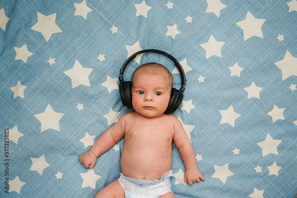 Bebe escuchando musica con cascos inalambricos sobre la cama con estrellas
