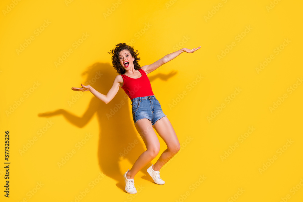 Full length body size photo of funny female student with curly hair dancing at university party singing standing tiptoes isolated on vivid yellow color background