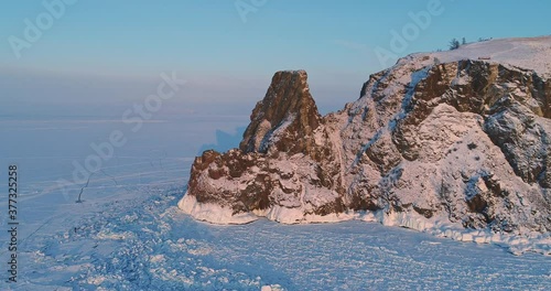 Aerial view of Shamanka rock and Cape Burkhan at sunset on frozen lake Baikal, Olkhon island in winter. Khuzhir, Siberia, Russia. Landscape of Russian natural landmark. 
