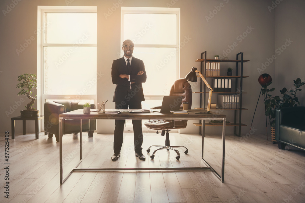 Full length photo of handsome dark skin business boss man guy notebook table standing self-confident hands crossed wear luxury suit tuxedo modern interior office indoors