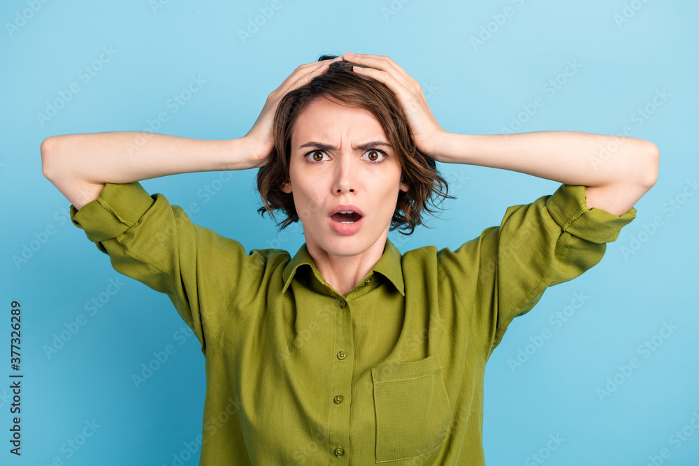 Portrait photo of nervous confused afraid girl with short brunette hair keeping head with both hands starring with opened mouth isolated on blue color background Portrait photo of nervous confused afraid girl with short brunette hair keeping head with both hands starring with opened mouth isolated on blue color background