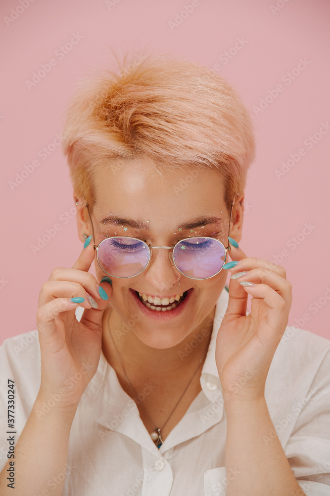 Shy happy young woman with short blond hair, round glasses and stars eye makeup