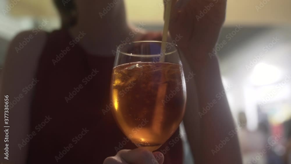 Selective focus as a woman mixing, blending drink with a straw. Log, ungraded footage. Waiting on a date concept. Selective focus as a woman mixing, blending drink with a straw. Log, ungraded footage. Waiting on a date concept.
