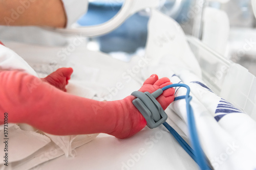 Premature baby foot with a neonatal pulse oximetry monitor, selective focus. Small newborn is placed in a premature newborn incubator. Neonatal intensive care unit