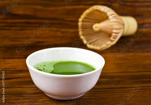 Matcha tea in a white cup with bamboo matcha tea whisk also know as chasen on a wooden background.