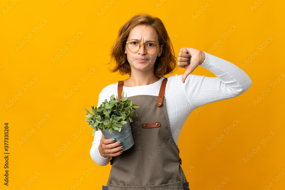 Young Georgian woman holding a plant isolated on yellow background showing thumb down with negative expression Young Georgian woman holding a plant isolated on yellow background showing thumb down with negative expression