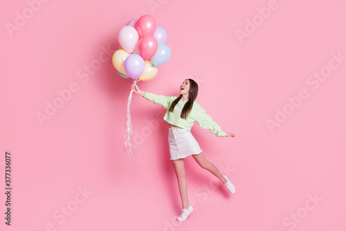 Full body photo of surprised shocked crazy cheerful girl hold many air balloons fly air impressed enjoy rejoice wear white sweater sneakers isolated pastel color background