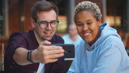 Young man and woman taking selfie on smartphone relaxing in outdoors cafe