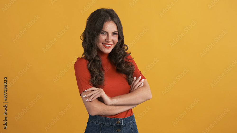 Beautiful smiling girl in red top with hands crossed confidently looking in camera over colorful background Beautiful smiling girl in red top with hands crossed confidently looking in camera over colorful background