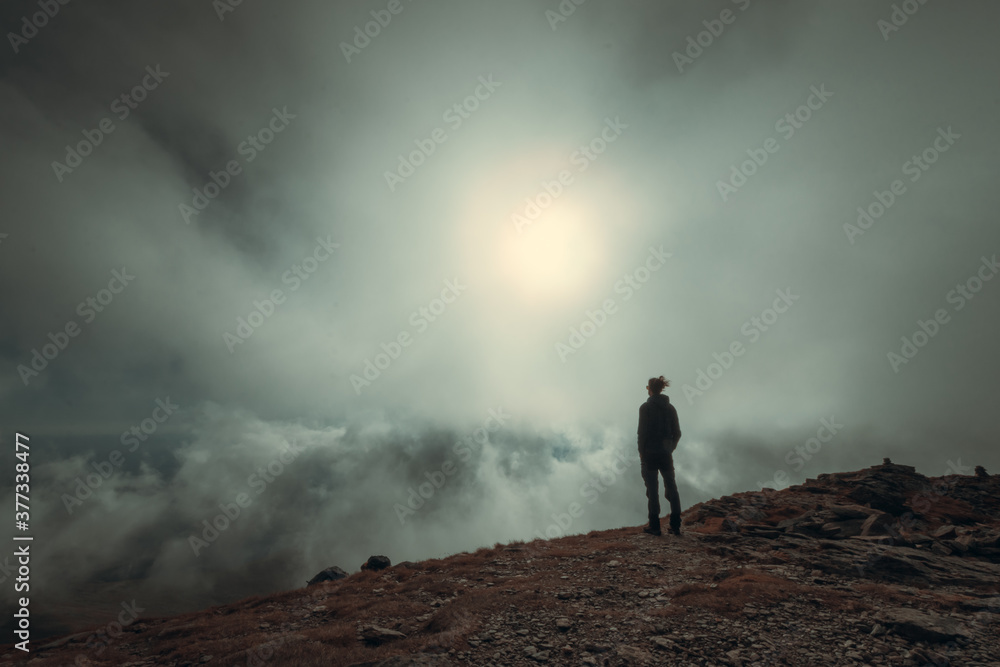 Man silhouette standing in front of sun and fog on the mountain