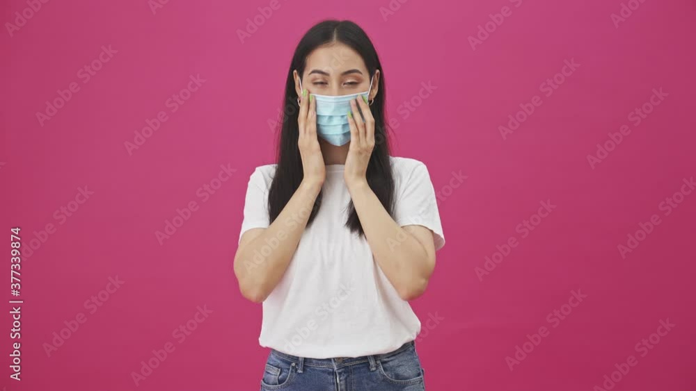 A pretty young woman is putting on protective mask standing isolated over a pink background A pretty young woman is putting on protective mask standing isolated over a pink background