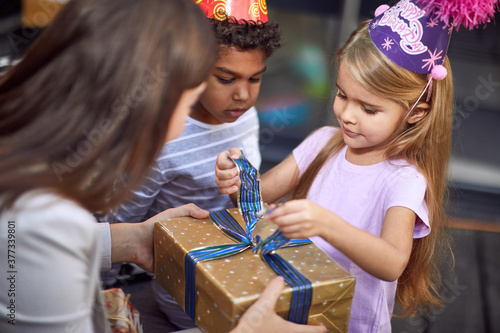 Foto caucasian girl unwrapping birthday present from young adult female with afro-ame
