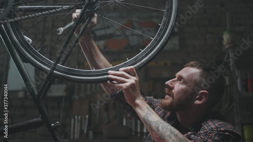 Male mechanic tighten screw on frame of bicycle with screwdriver. photo