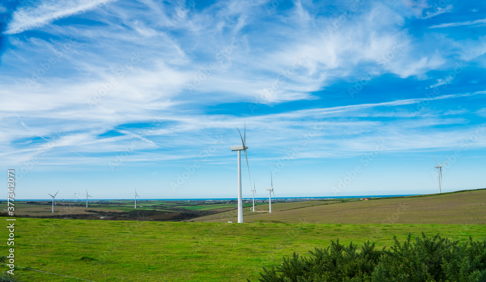 Wind turbine - renewable energy source on green meadows with sea on horizon. The concept of environmental protection and friendly use. Modern equipment for generating electric energy. Modern windmills Wind turbine - renewable energy source on green meadows with sea on horizon. The concept of environmental protection and friendly use. Modern equipment for generating electric energy. Modern windmills