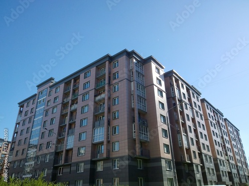 Facade of new multi-story residential building. Blue sky background. House Share. Real estate investing. Buy, sale, rental and insurance of economy class apartments in crisis. Housing development