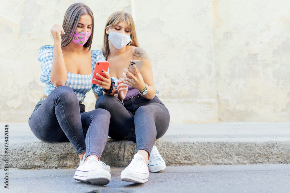 Naklejka premium serious women with a face mask looking at a smart phone, checking the news on a street curb
