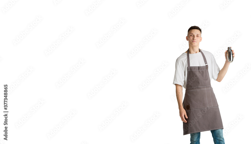 Holding shaker, smiling. Portrait of a young male caucasian barista or bartender in brown apron. Studio background, copyspace. Beautiful young man. Professional occupation, drink, service. Flyer Holding shaker, smiling. Portrait of a young male caucasian barista or bartender in brown apron. Studio background, copyspace. Beautiful young man. Professional occupation, drink, service. Flyer