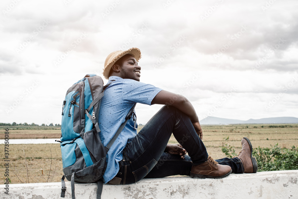 African traveler man sitting and lying with backpack on view of mountain background African traveler man sitting and lying with backpack on view of mountain background