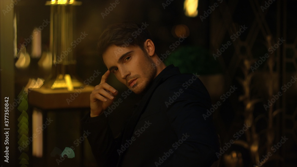 Pensive boss sitting in dark room. Young man touching face in blurred background