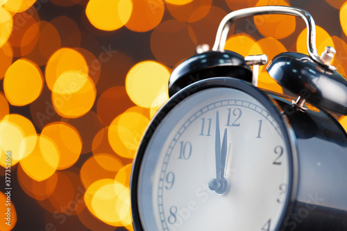 New Year eve concept with alarm clock against blurred garland