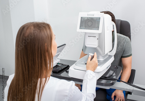 Female doctor looking very carefully at screen of ophthalmic autorefractor to correctly check the man’s vision. Vision correction
