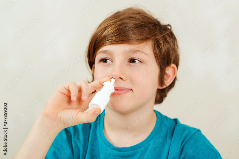 Sick school boy with runny nose using nasal medicine spray. Boy has a virus, runny nose and headache. Sick school boy with runny nose using nasal medicine spray. Boy has a virus, runny nose and headache.