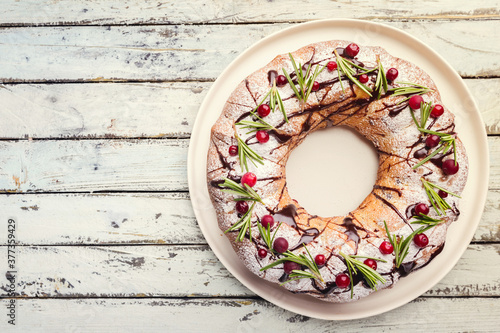 Cranberries bundt cake with chocolate and orange on a white plate. Homemade autumn and winter cozy holiday dessert on rustic wooden table, top view