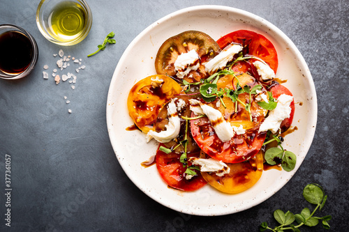 Fresh colorful tomatoes salad with mozzarella and balsamic vinegar on a plate, top view