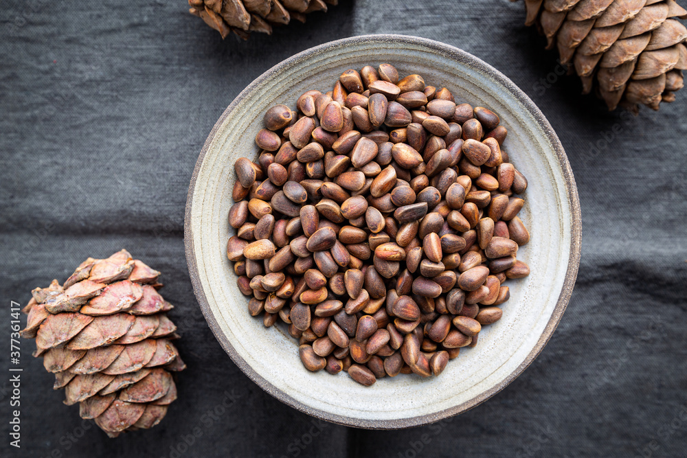 Cedar or pine nuts in a bowl with cones on gray background, top view Cedar or pine nuts in a bowl with cones on gray background, top view