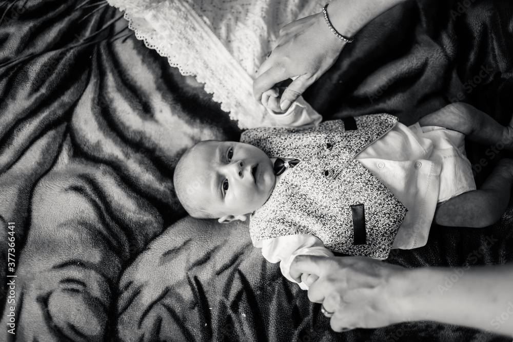 Black and white photo baby boy on a bed. Mother dresses newborn child in suit for christening Black and white photo baby boy on a bed. Mother dresses newborn child in suit for christening