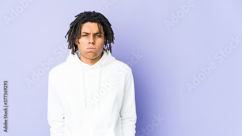 Young african american rasta man blows cheeks, has tired expression. Facial expression concept.