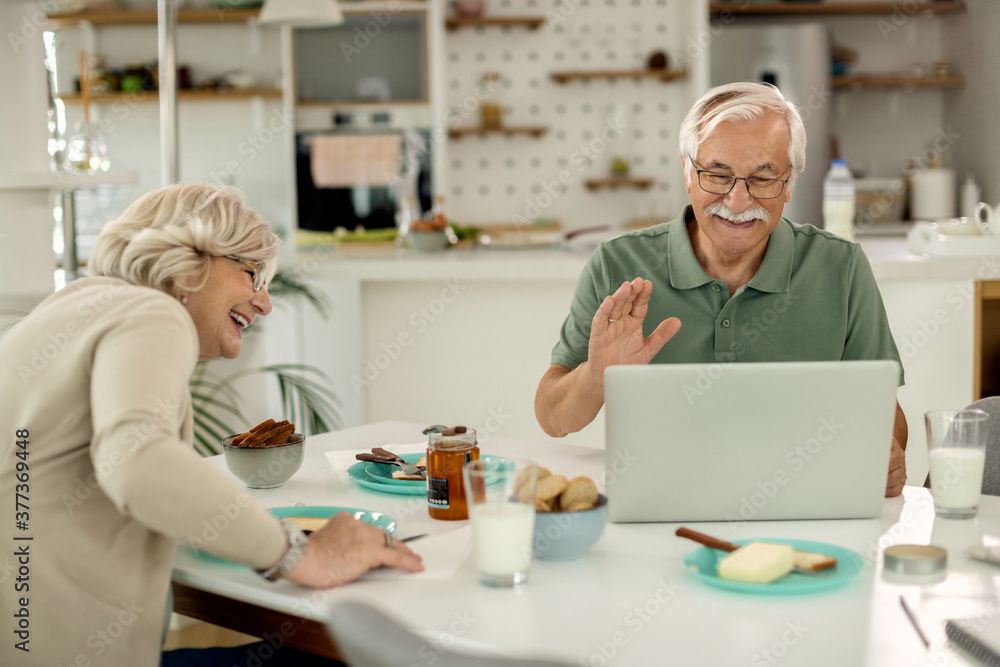 Obraz premium Happy senior couple making video call over laptop while having breakfast at home.