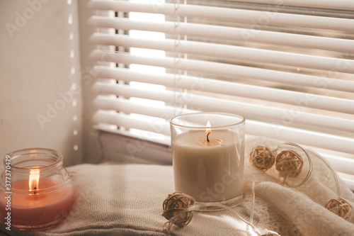 A cozy and warm hygge concept with white sweaters, candles, a cup, a garland on the windowsill. Autumn trends