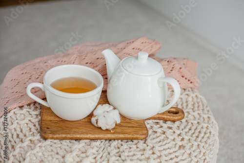 A mug of hot tea, a teapot, knitted sweater, a wooden stand on an ottoman. Cozy autumn. Winter breakfast. Cotton.