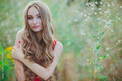 Portrait of a young beautiful girl in a red dress on the summer field outdoors