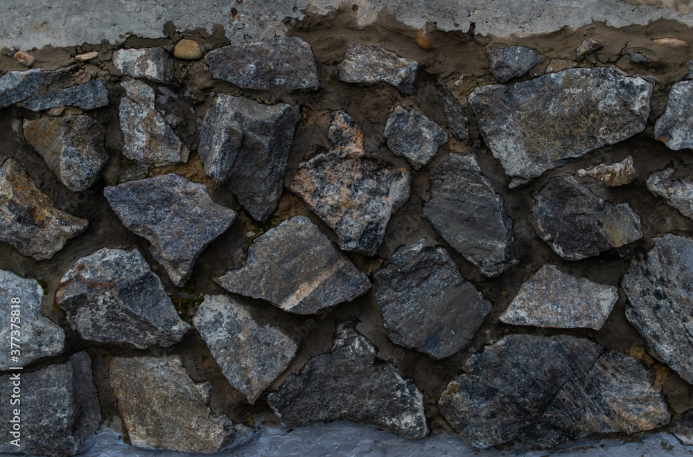 gray blue textured stone in rough cement in a sloppy wall with cracks, the work of builders, a rustic fence