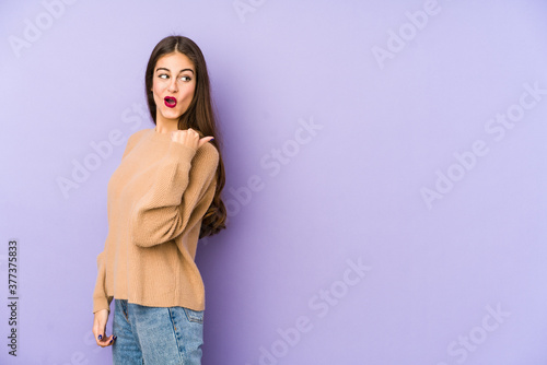 Young caucasian woman isolated on purple background points with thumb finger away, laughing and carefree. © Asier