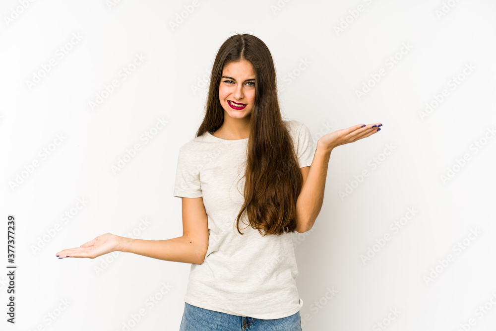 Young caucasian woman isolated on white background confused and doubtful shrugging shoulders to hold a copy space. Young caucasian woman isolated on white background confused and doubtful shrugging shoulders to hold a copy space.