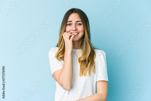 Young caucasian woman isolated on blue background biting fingernails, nervous and very anxious.