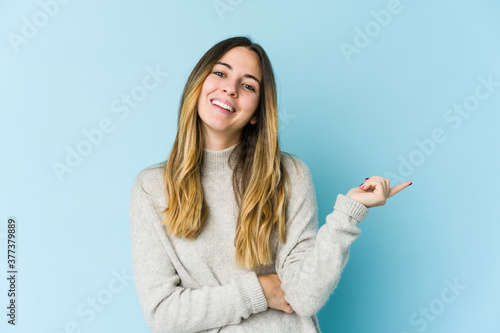 Young caucasian woman isolated on blue background smiling cheerfully pointing with forefinger away.