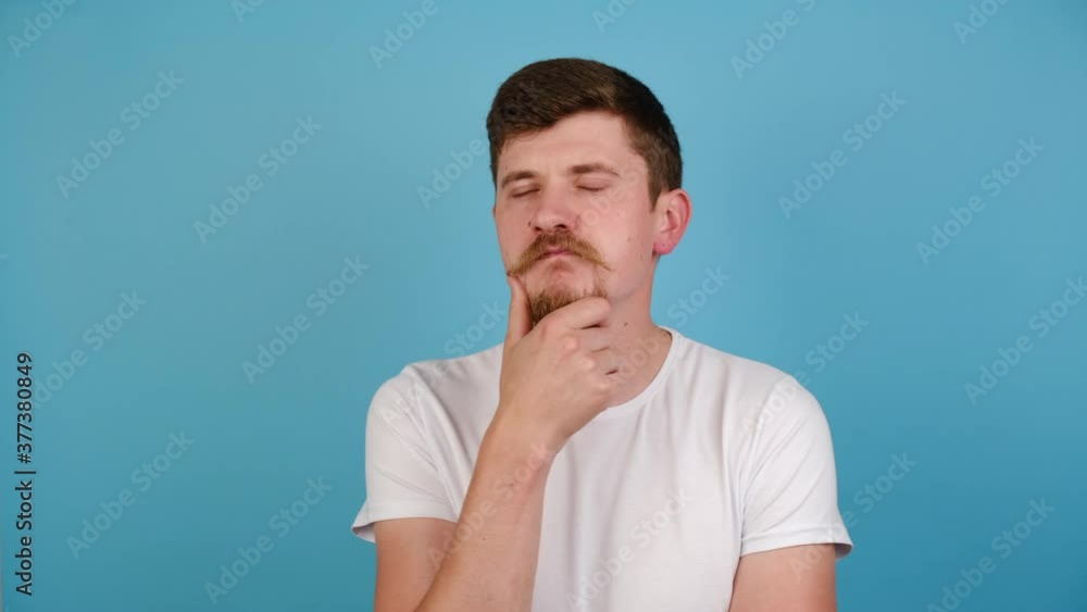 Thoughtful confused young man touching chin, scratching head while thinking over solution, millennial guy having doubts about difficult choice, wears white t-shirt, isolated on blue studio background Thoughtful confused young man touching chin, scratching head while thinking over solution, millennial guy having doubts about difficult choice, wears white t-shirt, isolated on blue studio background