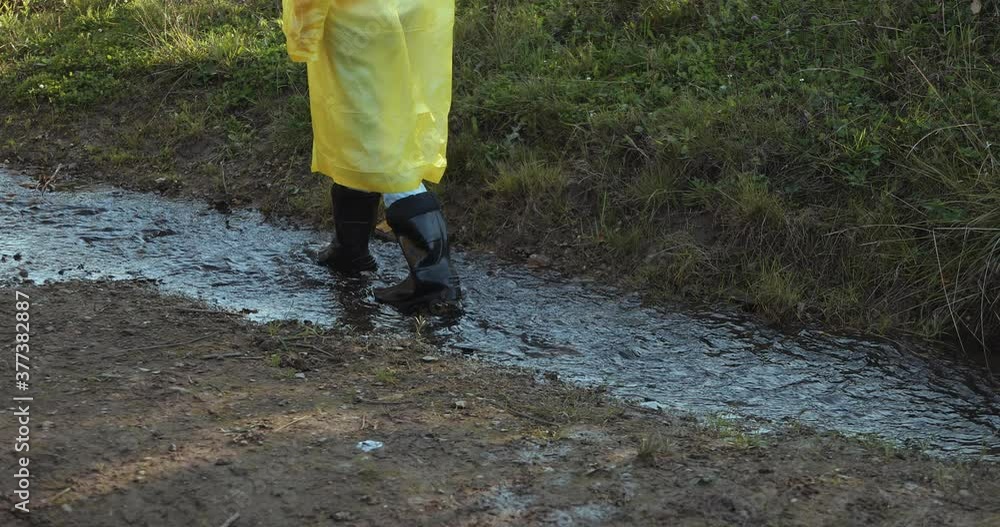 woman in a yellow raincoat and rubber boots jumping through puddles woman in a yellow raincoat and rubber boots jumping through puddles