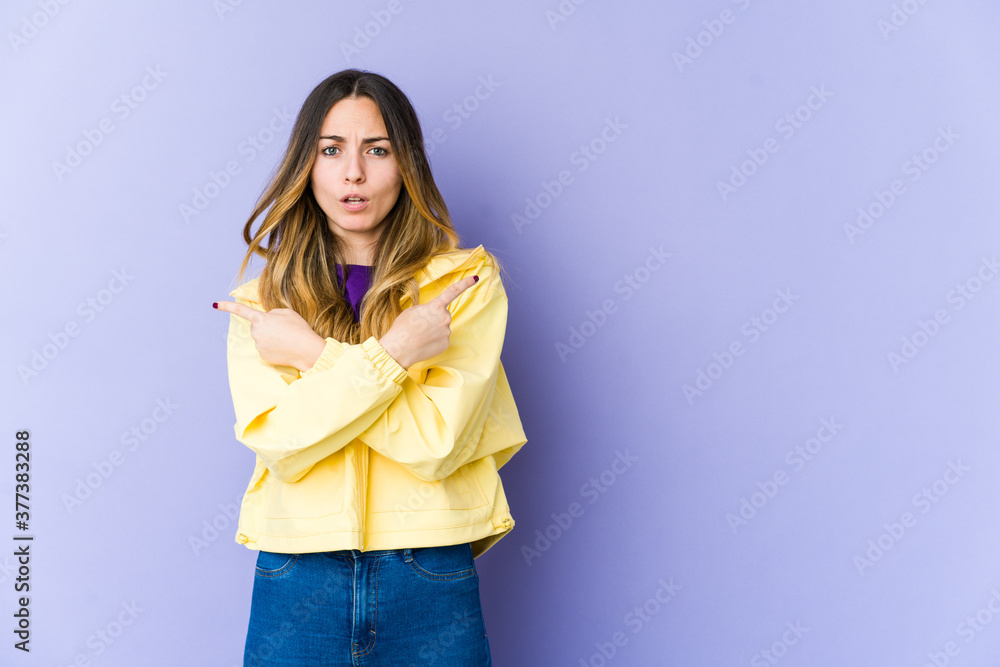 Young caucasian woman isolated on purple background points sideways, is trying to choose between two options. Young caucasian woman isolated on purple background points sideways, is trying to choose between two options.