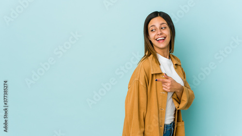 Young woman isolated on blue background looks aside smiling, cheerful and pleasant.