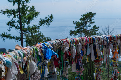 multicolored ribbons on the railing of the terrace against the backdrop of the landscape of blue lake Baikal, coniferous trees photo